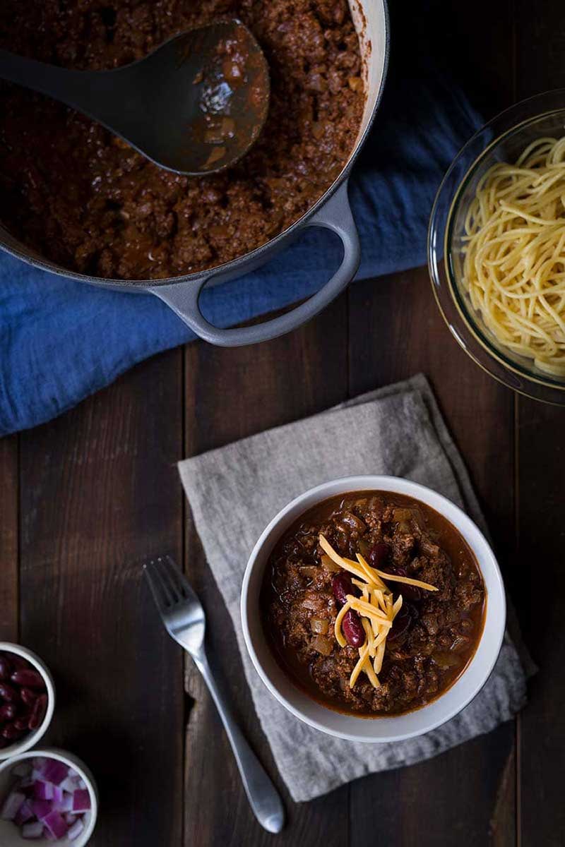 Cincinnati chili recipe in a bowl, surrounded by various toppings and a full batch of chili