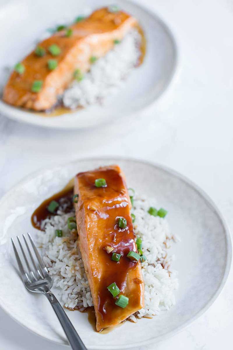 two baked teriyaki salmon filets on white plates with rice