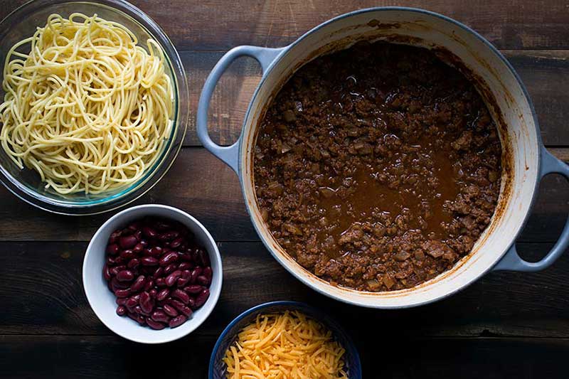 Cooked Cincinnati chili recipe in a Dutch oven, surrounded by classic garnishes.