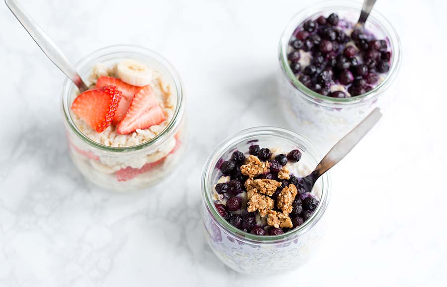 A photo of overnight oatmeal in individual serving jars, topped with strawberries, bananas, blueberries, and granola.