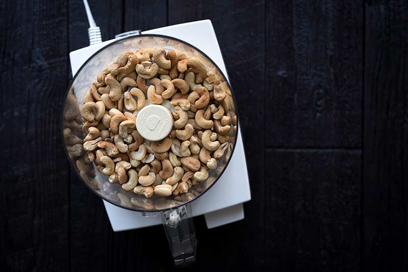Step-by-step photo showing how to make cashew butter - whole roasted cashews in a food processor.