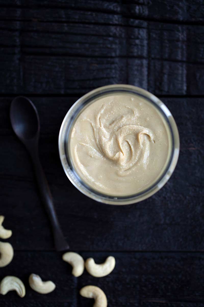 Homemade cashew butter in a jar next to cashews