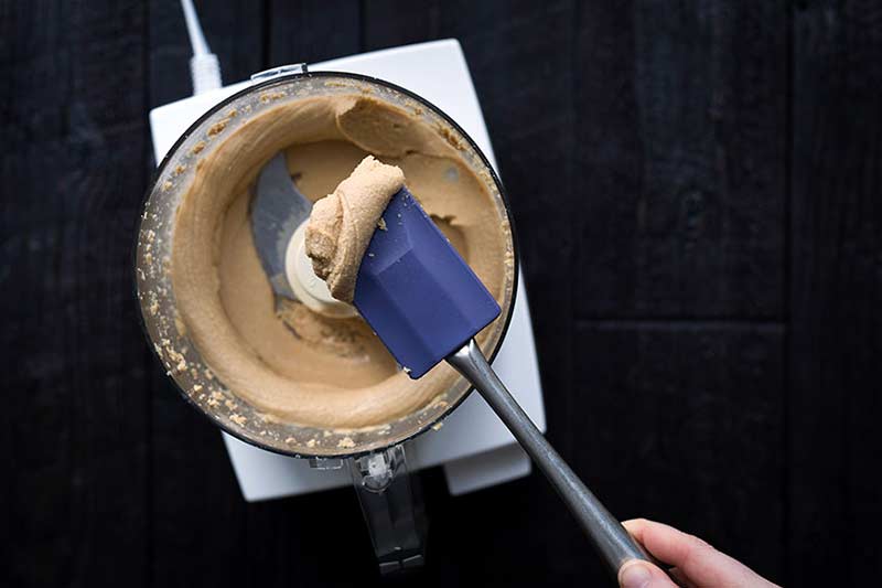 overhead photo of a creamy nut spread in the bowl of a food processor, with some on a spatula