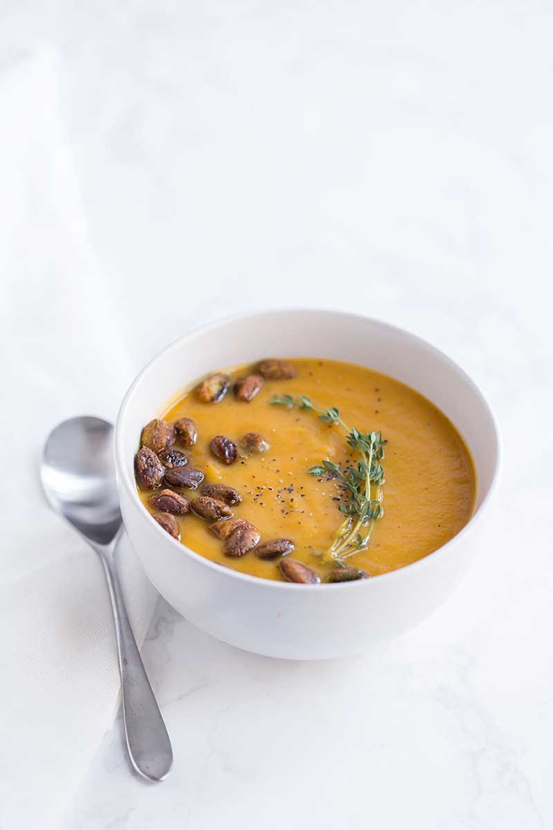 roasted butternut squash soup recipe garnished with pistachios, thyme, and black pepper