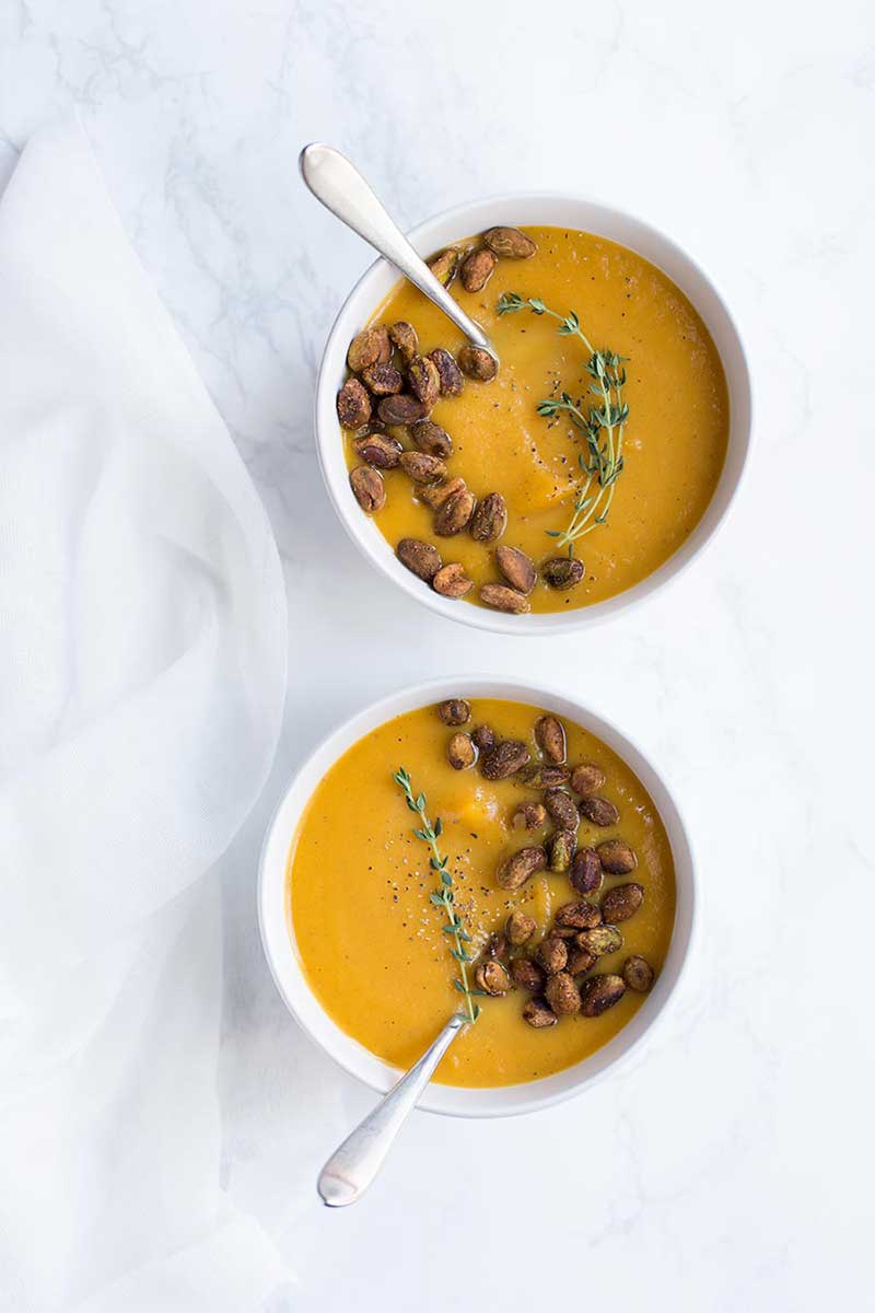 An overhead shot of vegan butternut squash soup garnished with nuts and thyme.