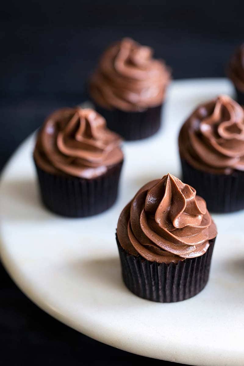 chocolate cupcakes from scratch displayed on a marble cake stand set against a dark backdrop