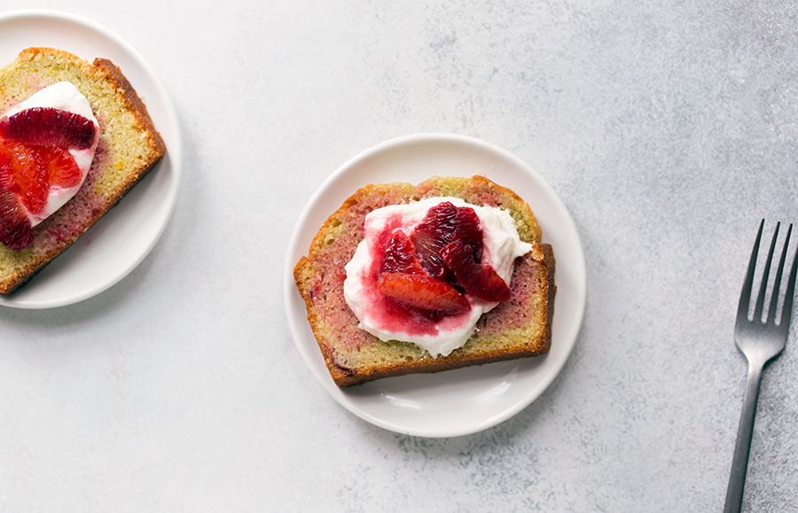A photo showing a slice of blood orange olive oil cake topped with whipped cream and orange segments.