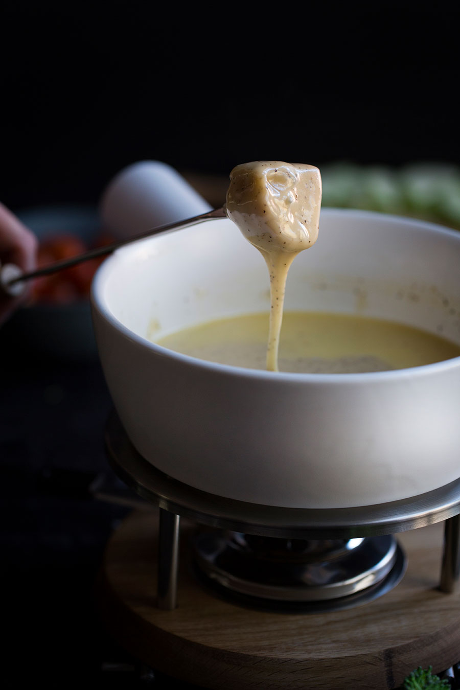 A closeup photo of gooey cheese fondue dripping off bread.