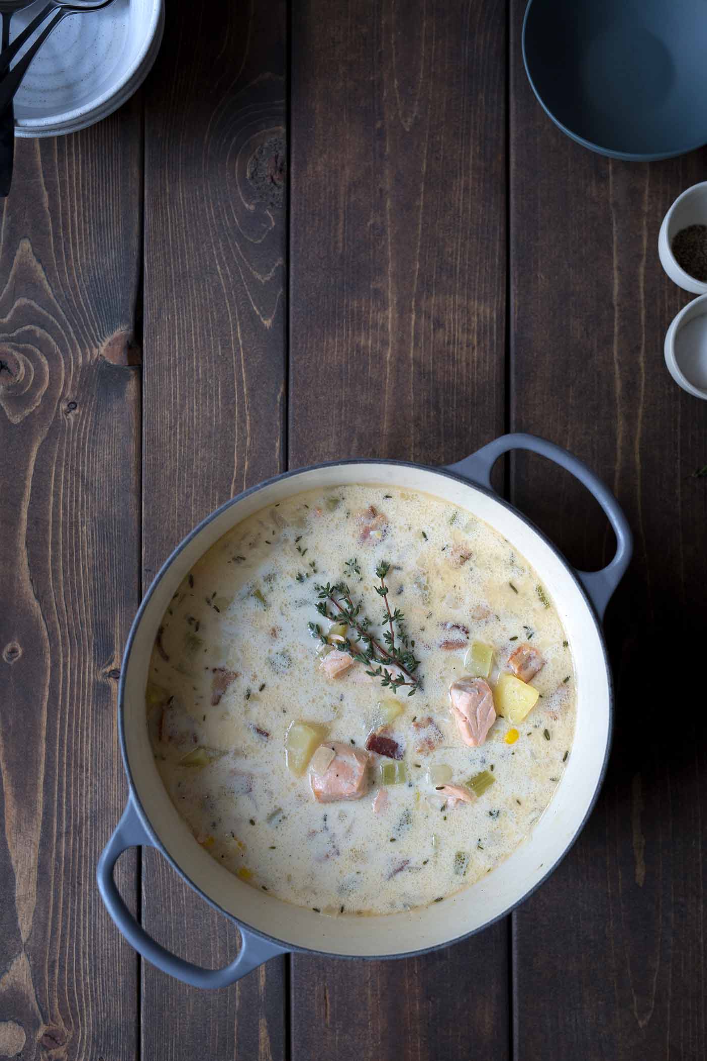 A photo of salmon chowder in a dutch oven, garnished with a sprig of fresh thyme