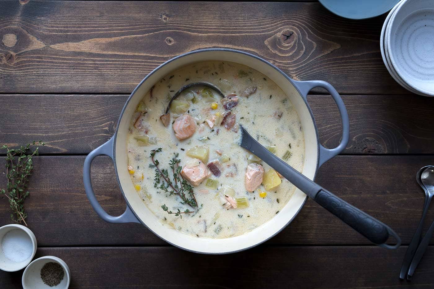 Salmon chowder in a large pot showcasing some of the various ingredients, including potatoes and bacon.