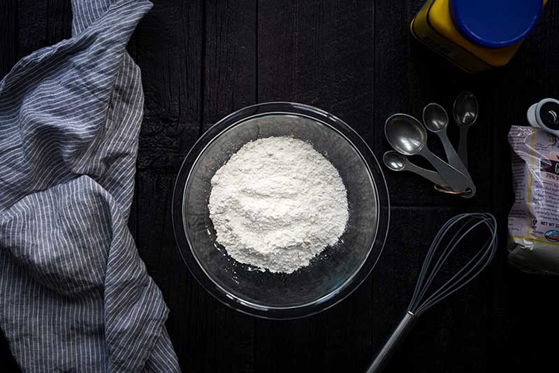 A photo of flour in a bowl next to a whisk.