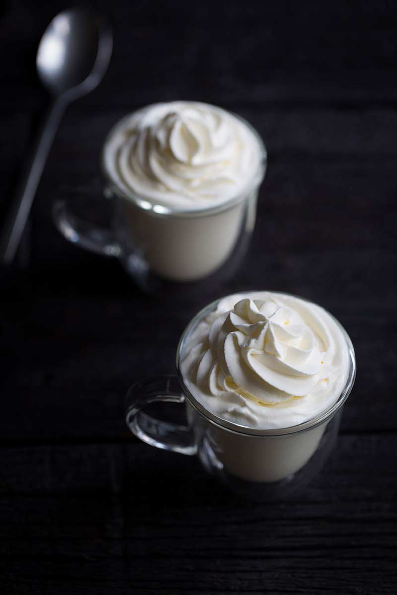 A close up photo of white hot chocolate on a dark backdrop.