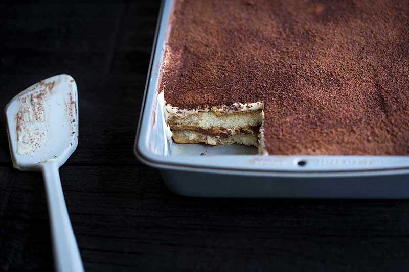 Tiramisu in a baking pan with one slice missing and a spatula