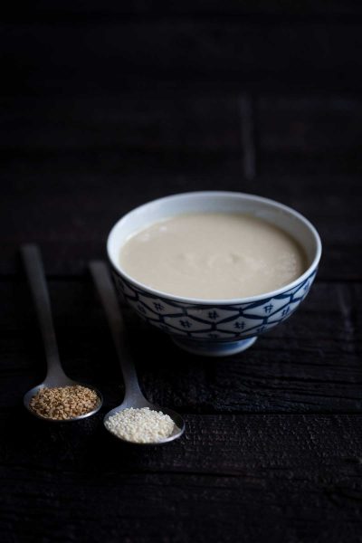 Homemade tahini in a bowl next to toasted and untoasted sesame seeds