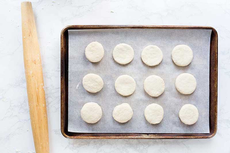 A sheet pan lined with parchment paper, topped with 12 raw buttermilk biscuits.