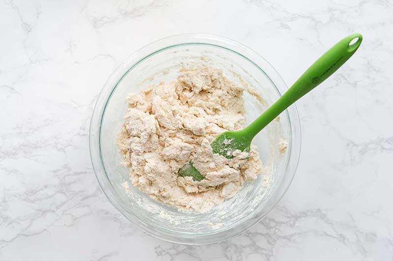 Biscuit recipe ingredients in a bowl, just barely stirred together with a green spatula.