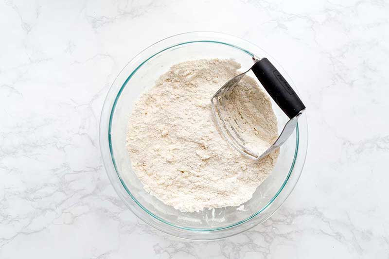 Combining biscuit recipe ingredients in a bowl with a pastry blender to keep the butter cold.