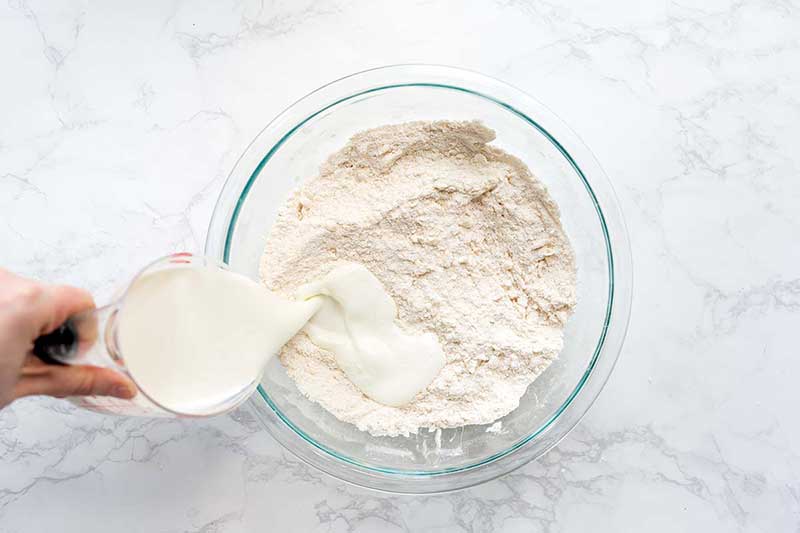 Action shot of buttermilk being added to a bowl with other biscuit ingredients.