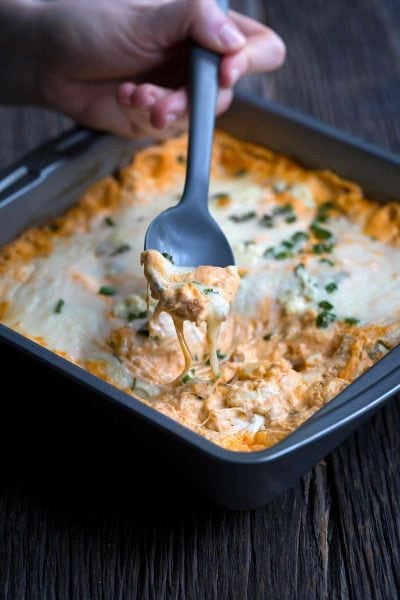 Buffalo chicken dip being scooped with a spoon. Oozing cheese dripping back into the pan.