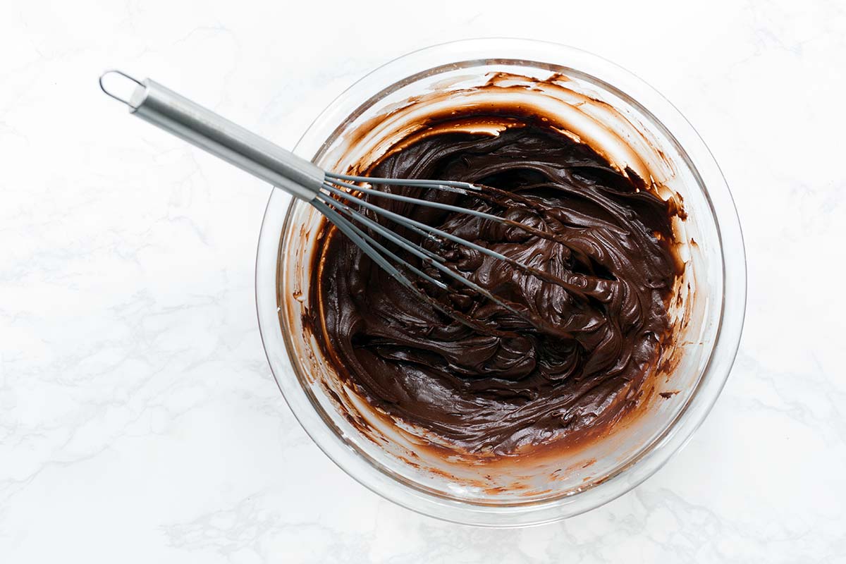The finished sour cream chocolate frosting in a bowl with a whisk.