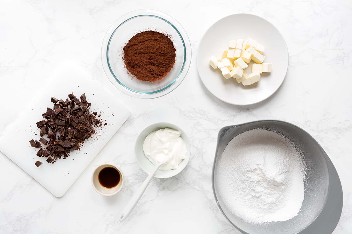 Ingredients for chocolate frosting, including powdered sugar, butter, sour cream, chocolate, cocoa powder, and vanilla.