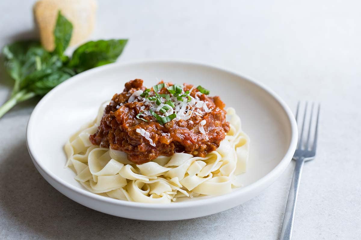 A photo of Italian meat sauce in a bowl, served over pasta and topped with cheese and basil. 