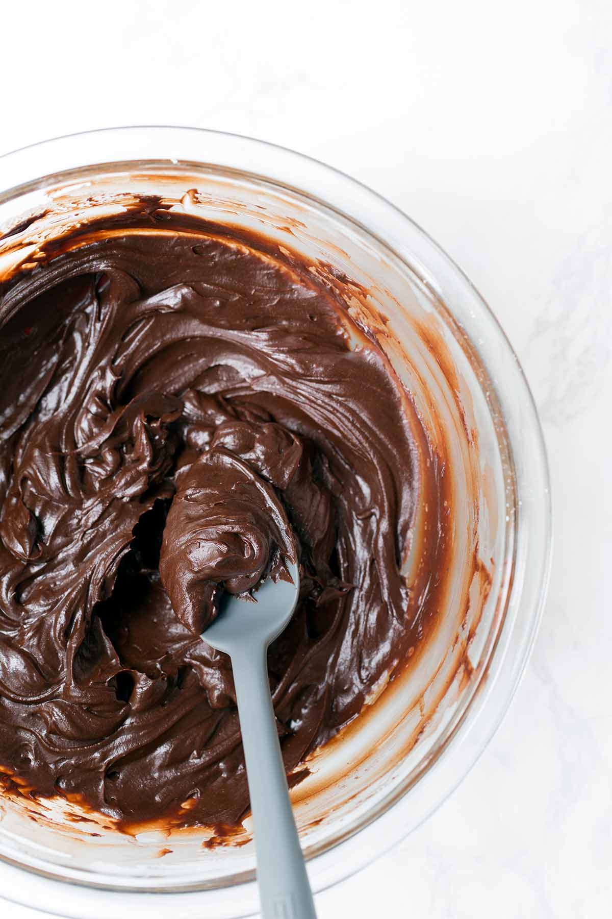 Close up photo of a bowl of chocolate sour cream frosting with a spoon.