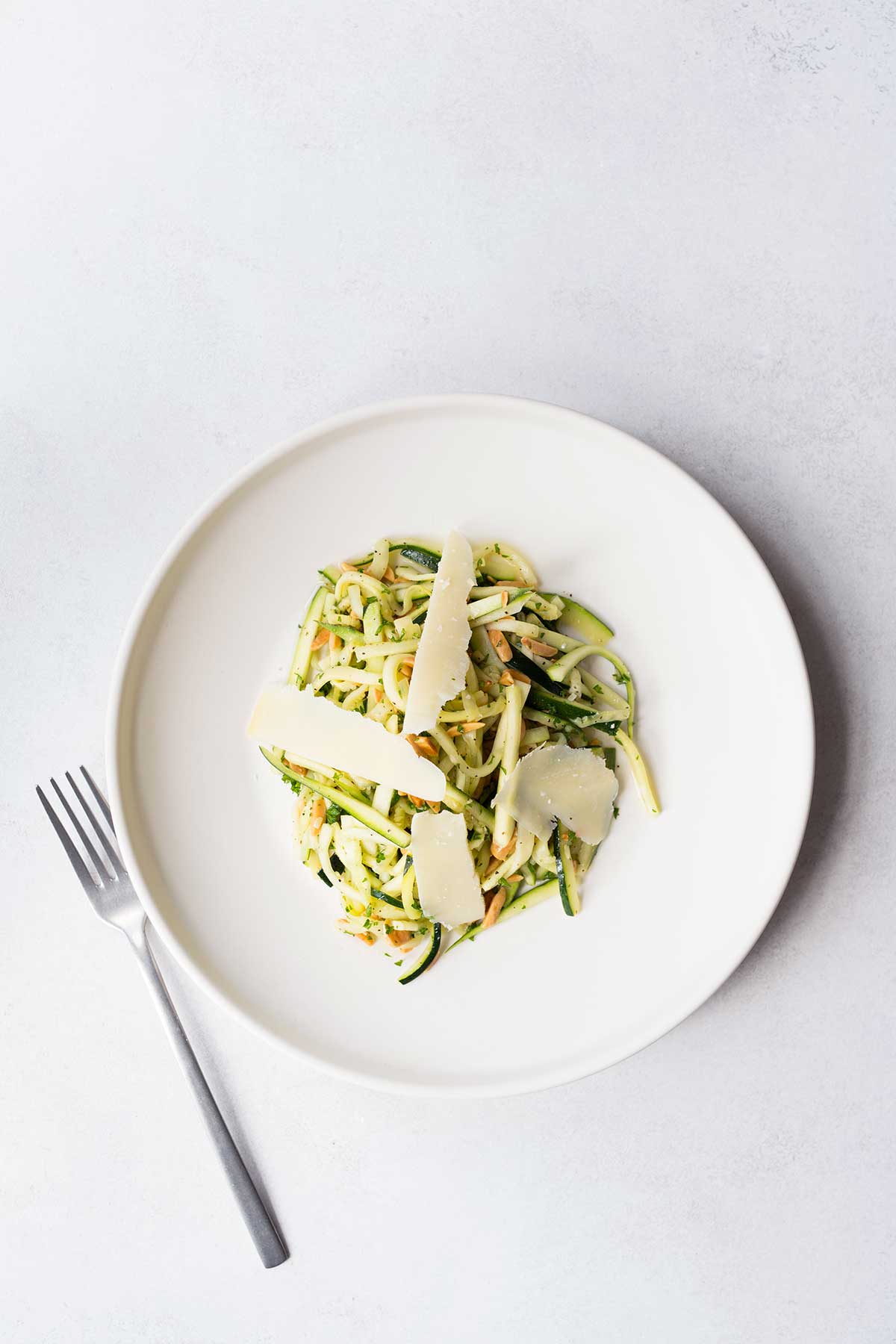 Lightly cooked zucchini mixed with almonds, parsley, and shaved gruyere, tossed with olive oil and lemon juice. Served on a plate.