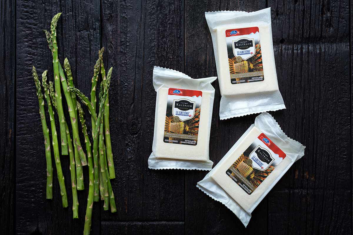 Emmi USA's Kaltbach Le Gruyére next to several stalks of fresh, seasonal asparagus.