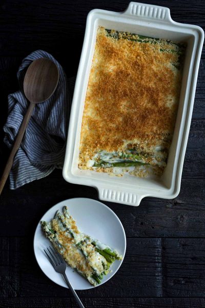 Asparagus gratin in a white casserole dish, next to one serving on a plate.