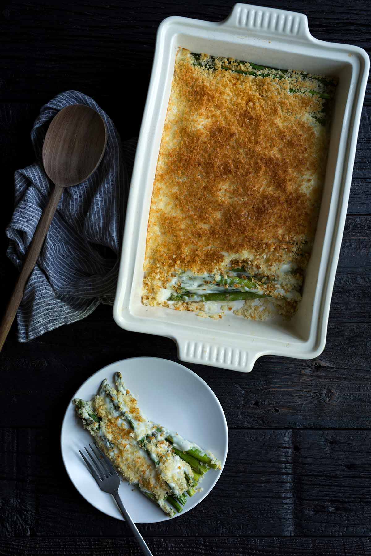 Asparagus gratin in a white casserole dish, next to one serving on a plate.