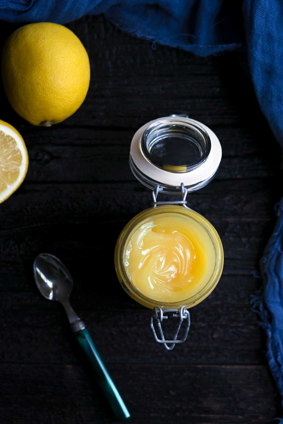 Homemade lemon curd in a mason jar, surrounded by fresh lemons.