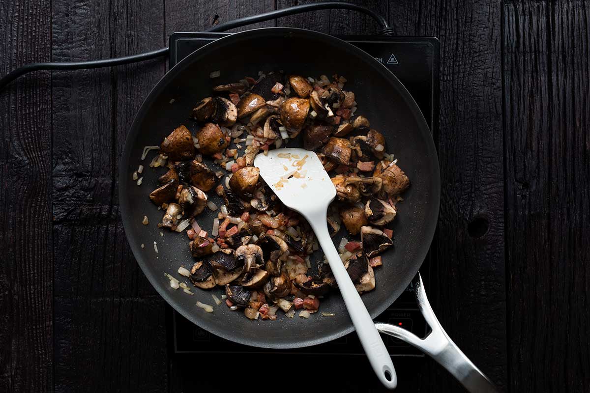A large skillet with pancetta, shallots and onions being cooked for chicken marsala sauce.