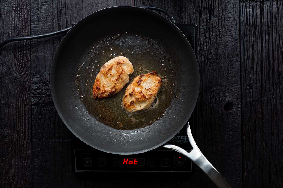 Chicken breasts pan frying in a large skillet.