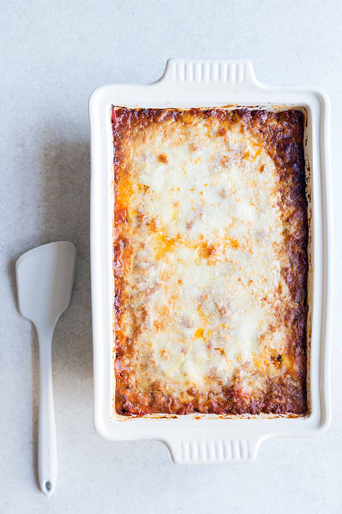A photo of zucchini lasagna in a casserole dish on a pale backdrop.