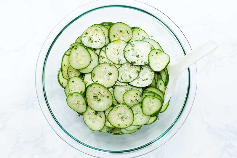 Thinly sliced cucumbers and chopped chives in a large pyrex bowl.