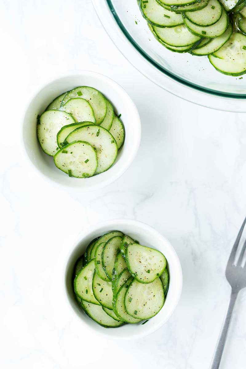 Two small white bowls and one large bowl showcasing cucumber salad.