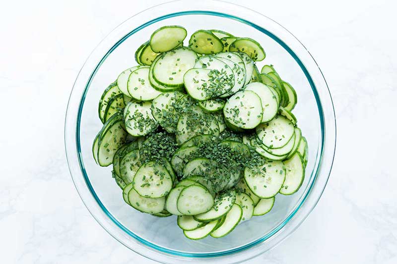 Thinly sliced cucumbers and chopped chives in a large pyrex bowl.