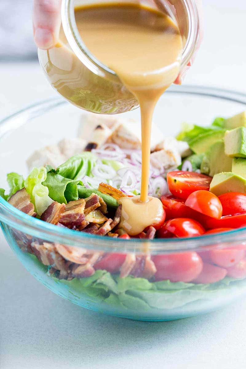 Honey mustard dressing being poured over a large salad.