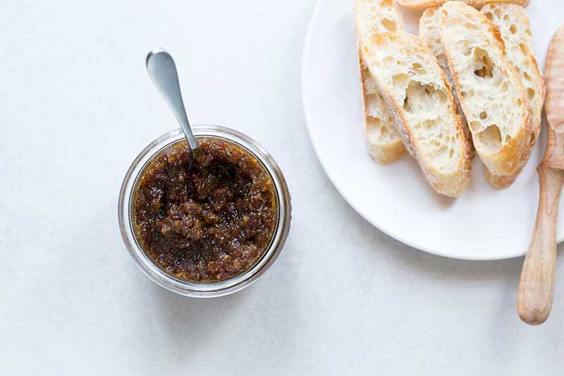 A spoon in a jar of bacon jam next to a plate of crostini.