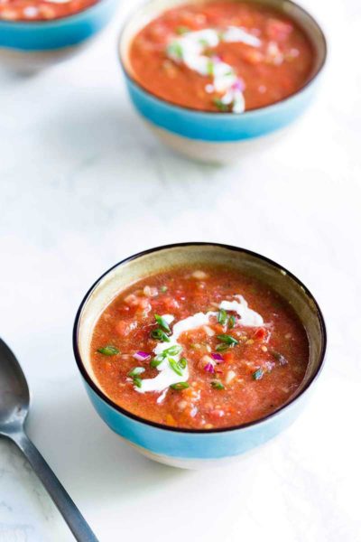 Tomato gazpacho soup in a blue bowl on a white backdrop.