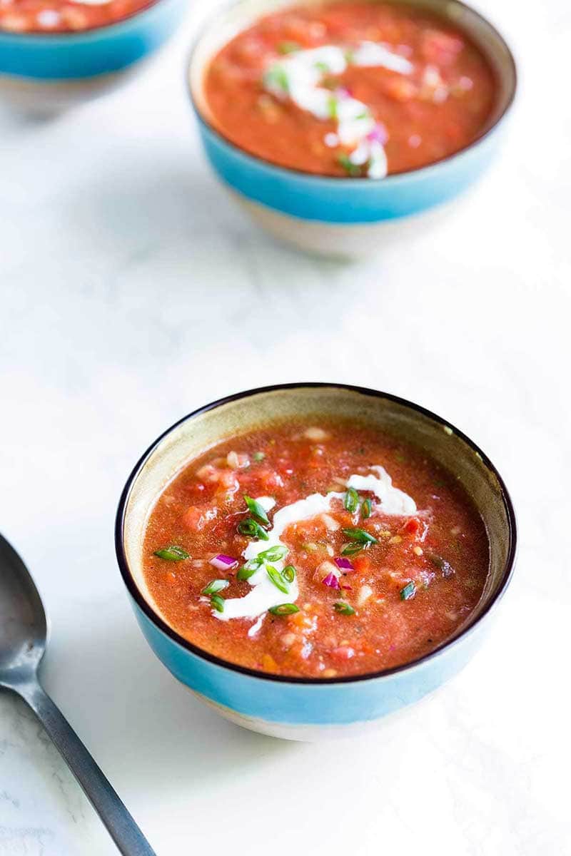 Tomato gazpacho soup in a blue bowl on a white backdrop.