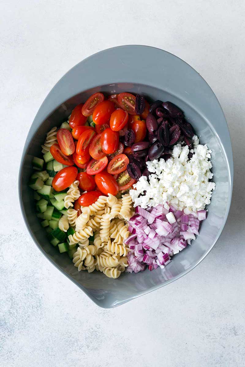 overhead image: ingredients in a stainless steel mixing bowl to make a Mediterranean pasta salad recipe