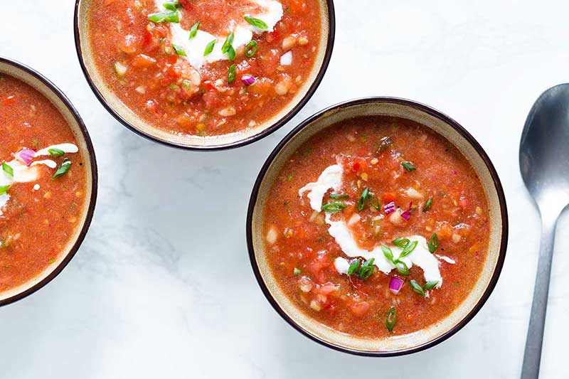 Three bowls of the best gazpacho recipe on a white marble backdrop.