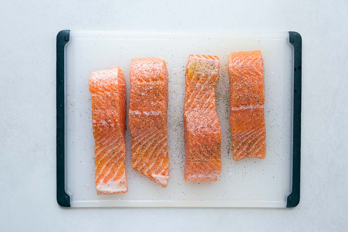 Four raw center-cut salmon fillets on a cutting board, seasoned with salt and pepper.