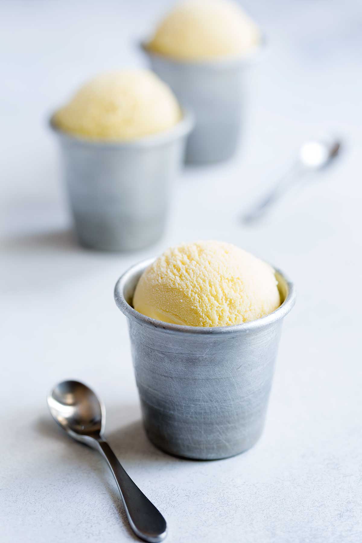 Buttermilk ice cream in aluminum cups, next to small silver spoons.