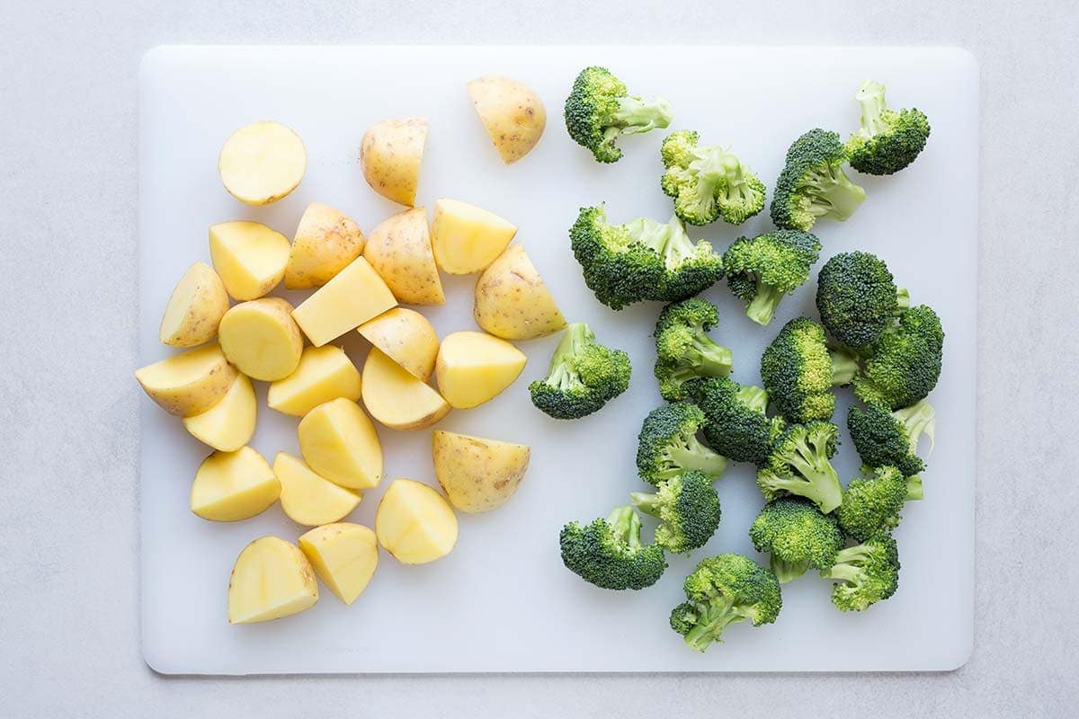 Yukon gold potatoes and broccoli florets cut to similar sizes, displayed on a cutting board.