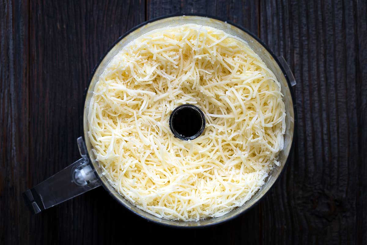 A food processor filled with cheese that has been shredded using the cheese attachment.