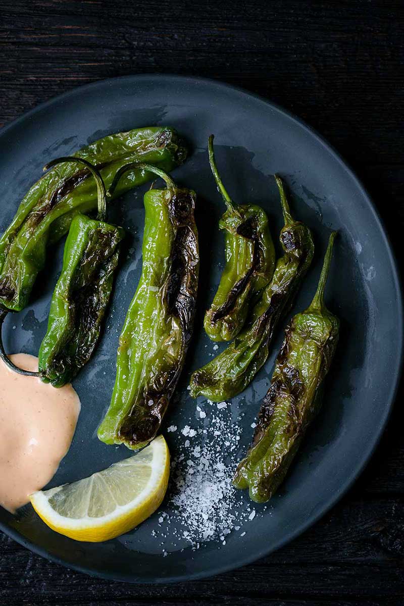 Blistered Shishito Peppers on a plate with coarse salt and sriracha aioli