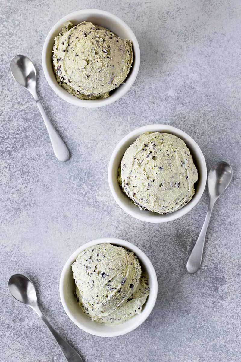three bowls of homemade mint chip ice cream and 3 spoons on gray marble background